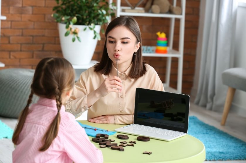 woman at table with girl showing a technique with mouth