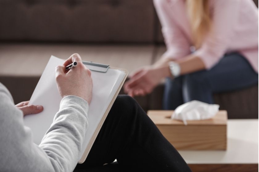 adult with clipboard and pen with a woman sitting on a couch